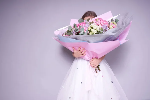 Дівчина в білій сукні стоїть збоку і тримає букет квітів, прикриваючи обличчя. Концепція свята — стокове фото