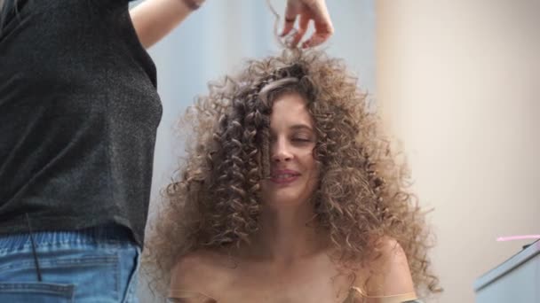 Close-up af en smuk kvinde med krøllet hår, hendes hår bliver gjort, hun griner ser på kameraet – Stock-video