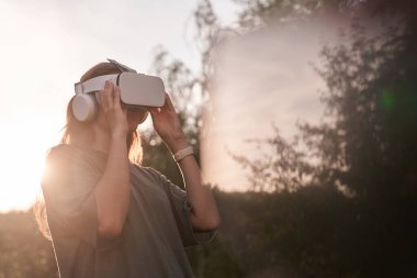 Elleriyle sanal gerçeklik kaskı tutan bir kız. Güneş ışığının yanında..