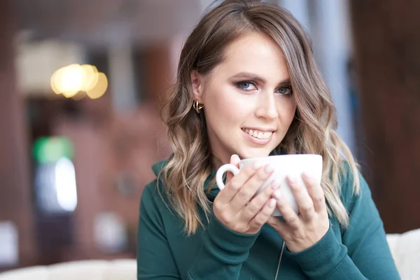 Güzel bir manikürlü, elinde fincanla bir kafede oturan güzel bir kadının yakın plan portresi. Kız doğrudan kameraya bakıyor. — Stok fotoğraf