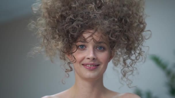 Au ralenti. Gros plan d'une belle jeune femme aux cheveux bouclés, elle regarde la caméra sourire, et ses cheveux tombent — Video