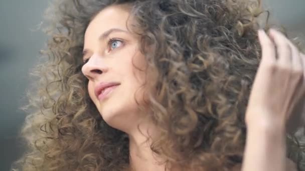 Primo piano di una bella donna con i capelli ricci, guarda la sua acconciatura allo specchio e ammira — Video Stock