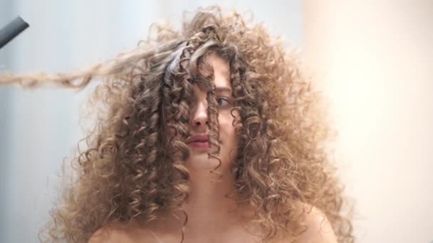 Close-up of a beautiful woman with curly hair, she gets her hair done, she looks at how a strand of hair is separated – Stock-video