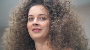 Kameraya bakan kıvırcık saçlı güzel bir genç kadının yakın çekimi. Efendi ona makyaj yapar, kaşlarını tarar.