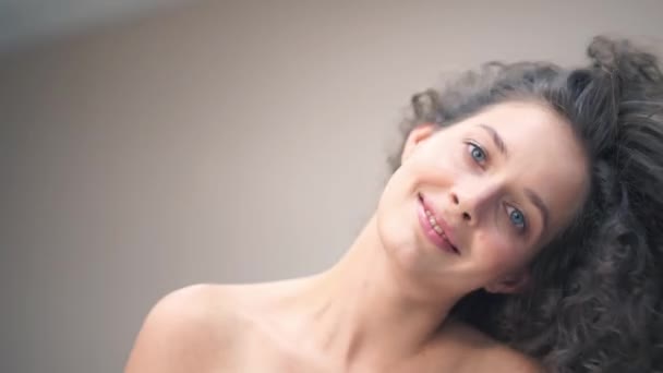 Close-up of a beautiful young woman with curly hair, she tilts her head in different directions, smiling at the camera, touching her hair with her hands — Stock video