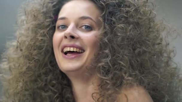 Close-up of a happy young woman with curly hair, makeup is applied to her, she looks at the camera and laughs — Stockvideo