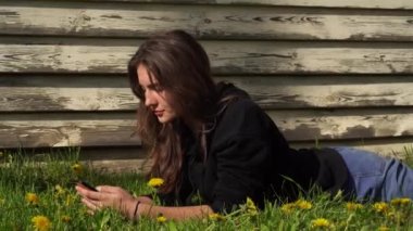 Gülümseyen genç bir kız parktaki yeşil çimlerin üzerinde yatıyor. Bir genç akıllı telefondan sosyal ağlarda mesajlaşıyor.