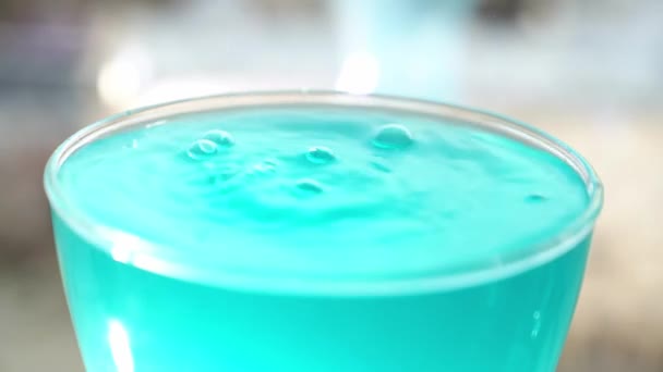 Giet water in een glas met turquoise water. In slow motion, een straal water giet in een glas vloeistof en maakt een plons op het oppervlak. — Stockvideo