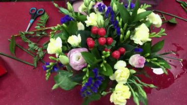 Çiçek atölyesi, farklı çiçeklerden buketler yapmak. Bir kadın bir buket çiçek topluyor. Çalışma sürecindeki insanlar.