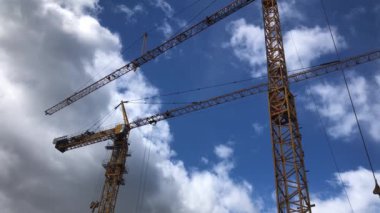 Mavi gökyüzünde iki sarı vinç, güzel bulutlar, inşaat işleri.