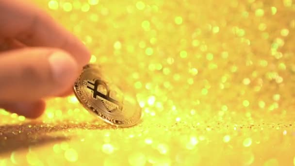Bitcoin on a shiny gold background in slow motion.Female fingers in close-up turn the bitcoin coin around its axis. — Stock Video
