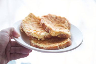 Beyaz bir tabakta kızarmış yumurtalı sandviç tabağını tutan bir elin yakın çekimi. Hızlı bir kahvaltı konsepti