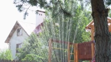 Bir yaz günü evin arka planına karşı çimleri sulayan fıskiyeye yakın çekim..