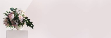 Banner, podyumun kenarında beyaz bir vazoda farklı renkte bir kompozisyon bulunmaktadır. Geometrik olarak boyanmış bir duvarın arkasında. Taze kesilmiş güzel bir buket.