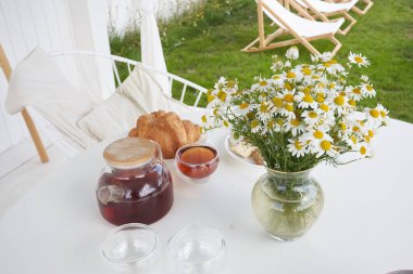 Masada çay ve bir vazo papatyayla taze kruvasan manzarası. Pazar kahvaltısı kır evinin arka bahçesinde..