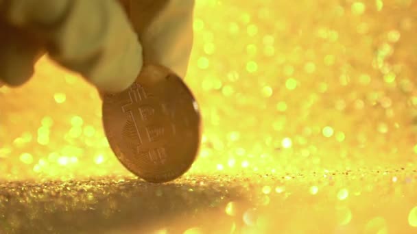 Female fingers in rubber gloves close-up rotate the bitcoin coin around its axis. A coin on a shiny yellow background in slow motion. — Stock Video
