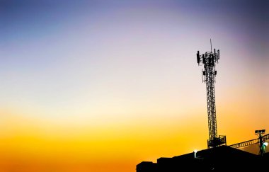 Akşamları güzel turuncu gökyüzü olan bir telefon iletişim kulesinin silüeti..