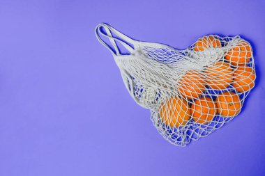 Mor bir arka planda, sicim torbasında mandalinalar. 