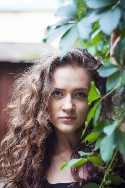 Attrayant fille est debout contre le mur avec des feuilles souriantes — Photo