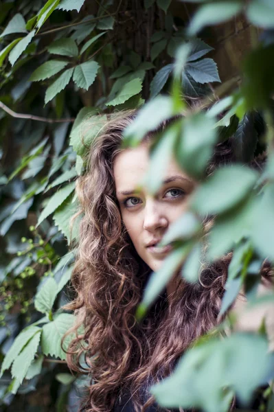 Attractive girl is standing against the wall with leaves smiling — Stock Photo, Image