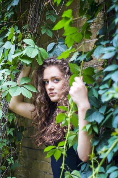 Attrayant fille est debout contre le mur avec des feuilles souriantes — Photo