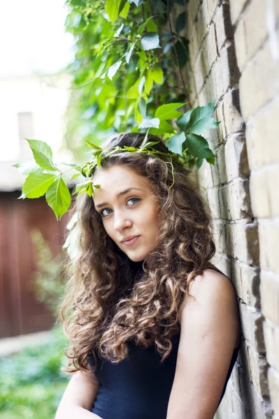 魅力的な女の子は笑みを浮かべての葉を持つ、壁に立っています。 — ストック写真