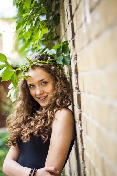 A vonzó lány áll a falnak, levelekkel, mosolyogva — Stock Fotó