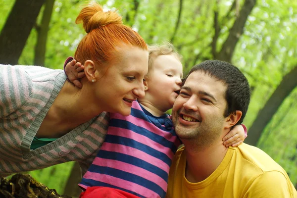 Happy mother and father kissing their daughter in the park — Stock Photo, Image