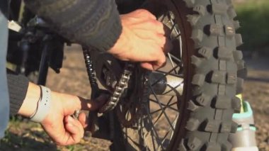 Adamın biri motosikletin zincirini tamir ediyor.