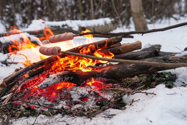 Sausages on the stick grilled in the fire. Winter forest.