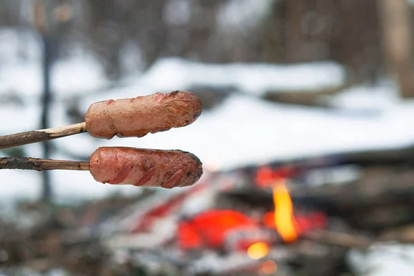 Sausages on the stick grilled in the fire. Winter forest