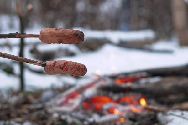 Sausages on the stick grilled in the fire. Winter forest