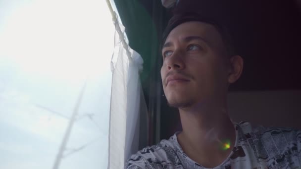 Retrato de un joven montado en un tren, mirando por la ventana. Enfoque selectivo — Vídeos de Stock