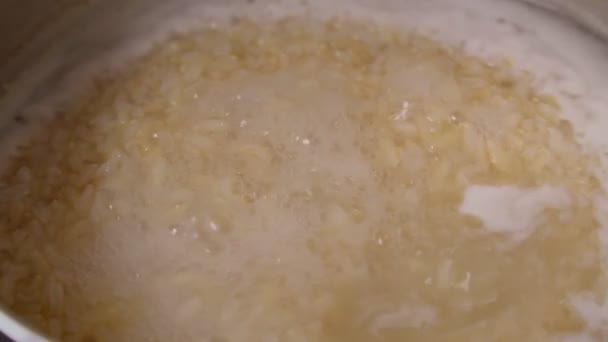 Cooking brown rice in a saucepan in hot water. Selective focus — Stock Video