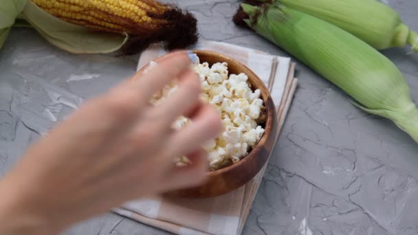 Мужские и женские руки берут попкорн. Чаша с вкусным традиционным попкорном и кукурузными початками на сером фоне — стоковое видео