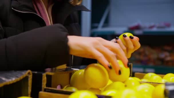 Руки девушки выбирают свежий лимон на полках гипермаркета. Селективный фокус — стоковое видео
