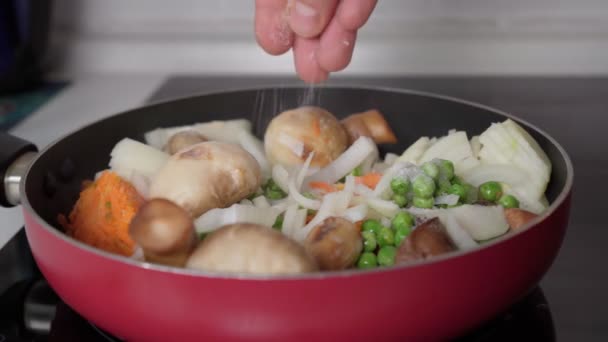 Cooking vegetables adding salt in a frying pan, mushrooms, peas, onions, carrots. Selective focus — Video Stock