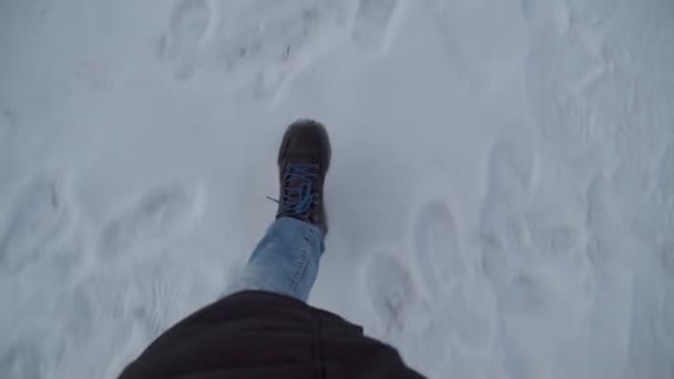 Legs of a man in black boots and jeans walking in the snow in winter. Pov video — Stockvideo