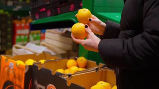 Жінка вибирає апельсин в руці в супермаркеті. Цитрусові фрукти є джерелом вітаміну С з берибером — стокове відео