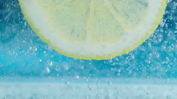 Nahaufnahme der Zitronenscheibe unter Wasser mit Blasen auf blauem Hintergrund. Zeitlupe — Stockvideo