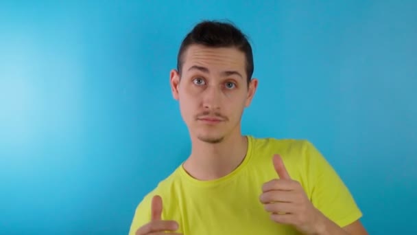Happy guy showing thumbs up. He is looking at camera against blue background. Slow motion — Stock Video