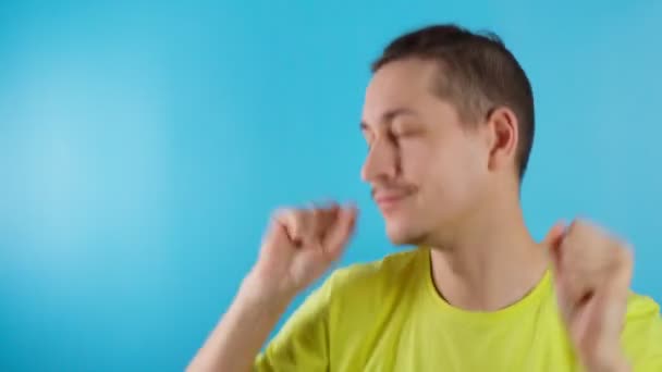 Смешной парень в жёлтой футболке на синем фоне танцует, веселится — стоковое видео