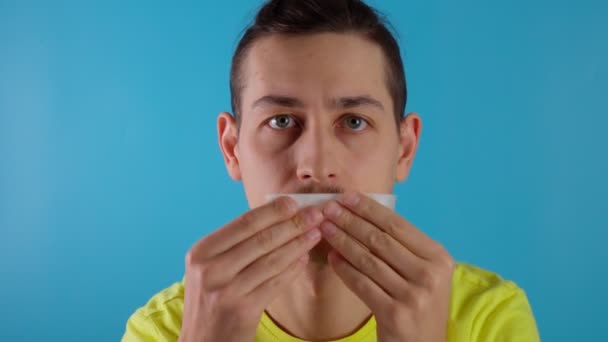 En ung tusenårig kille filmar sin mun stängd. Blå bakgrund. Förbud mot samtal — Stockvideo