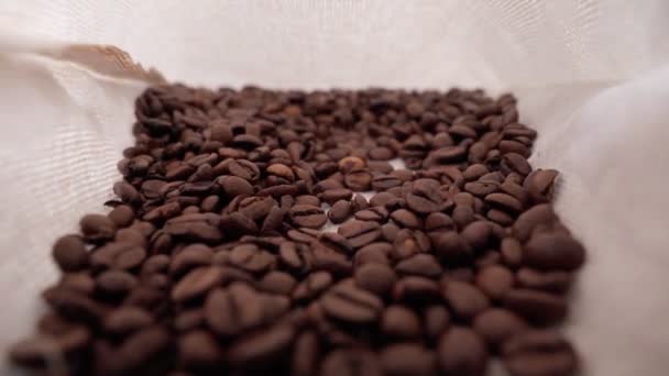 Roasted coffee beans pouring selective focus. Robusta variety inside the cloth bag. — Stockvideo