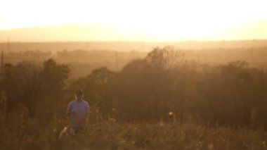 Ceketli ve başında kep olan bir genç kız tarlada üç köpekle yürüyor, köpeklerden ikisi tasmalı tutuluyor. Gün batımından önce, gökyüzü turuncu güneş ışığıyla doludur, ağır çekim.