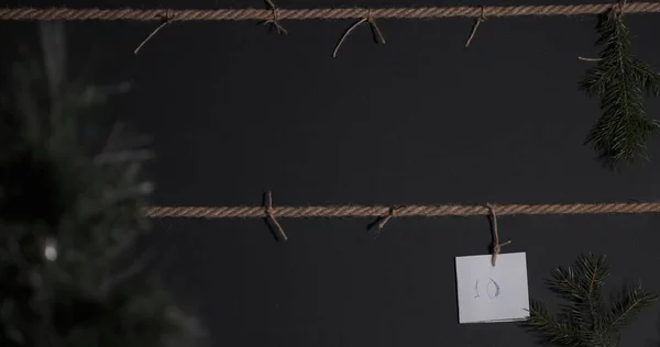 Ev yapımı DIY takvimi, siyah arka planda yaratıldı ve bir el işi teli ile bağlandı, ön planda çelenkli bir Noel ağacı var. Makas etiketlerden birini kesmek için uzanır