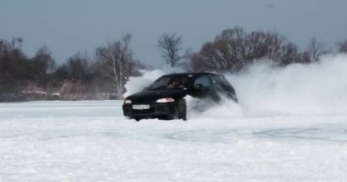 Spassk-Dalniy, Primorsky Krai, Rusya-2022 Ocak: Donmuş bir gölde, güneşli bir günde, karla kaplı bir otoyolda siyah bir araba sürüyor.