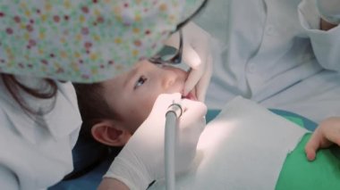 Kadın profesyonel dişçi iş başında. Dişçi muayenehanesinde, kadın diş hekimi klinikteki küçük bir çocuğa diş tedavisi yapıyor. Diş muayenesi kavramı.