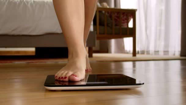 Vrouw is het meten van haar gewicht op de schalen.Meisjes voeten stap op de schalen.Vrouw benen staan op schubben in de kamer.Close-up vrouwelijke voeten controleren BMI gewichtsverlies. Barefoot man meten overgewicht vet — Stockvideo