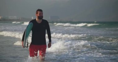 Sahilde sörf tahtası taşıyan yakışıklı yaşlı bir sporcunun portresi. Emekli bir sporcu denize girer, sörf tahtasıyla dalgalara biner..